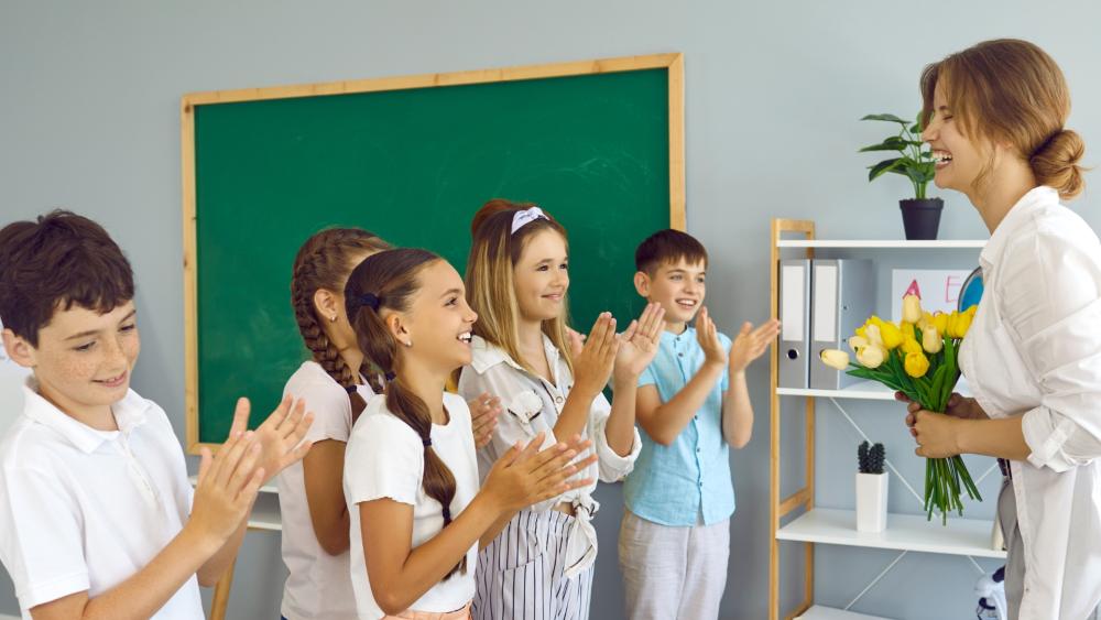 Bambini che applaudono la maestra delle elementari che viene in mano un mazzo di tulipani regalato da loro