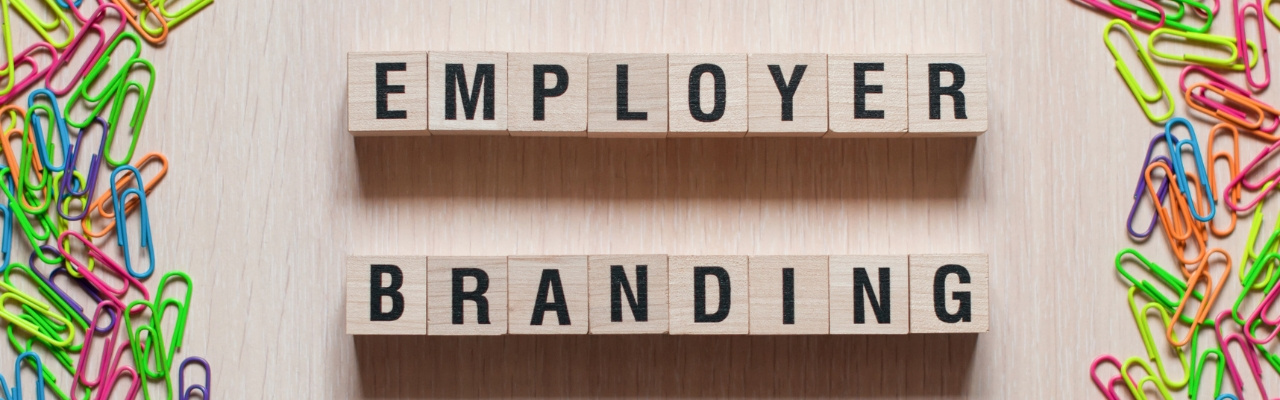 Cubi di legno che formano la scritta employer branding al centro di una cornice formata da graffette colorate poste a cornice