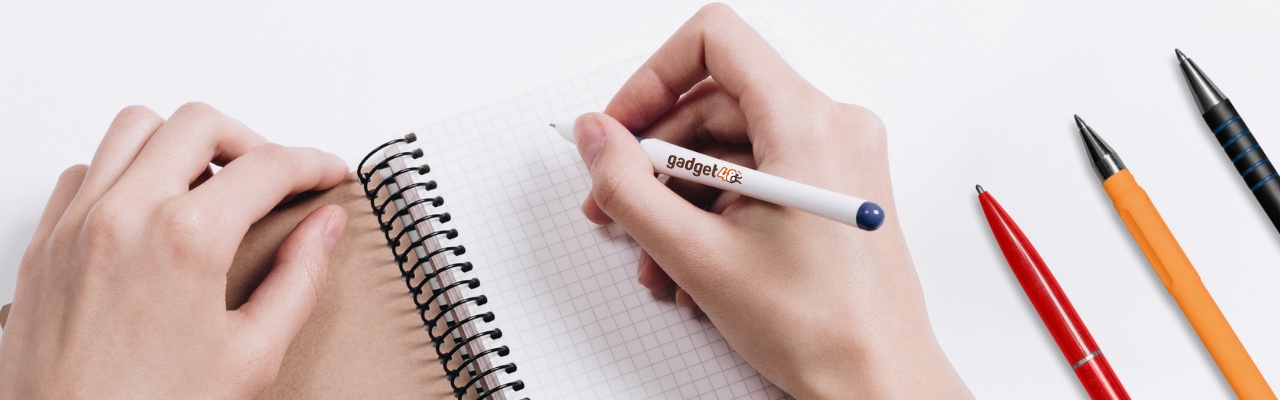 Mani che tengono una penna con logo di Gadget48.com per scrivere su un block notes aperto. Affianco altre 3 penne: una rossa, una gialla e una nera