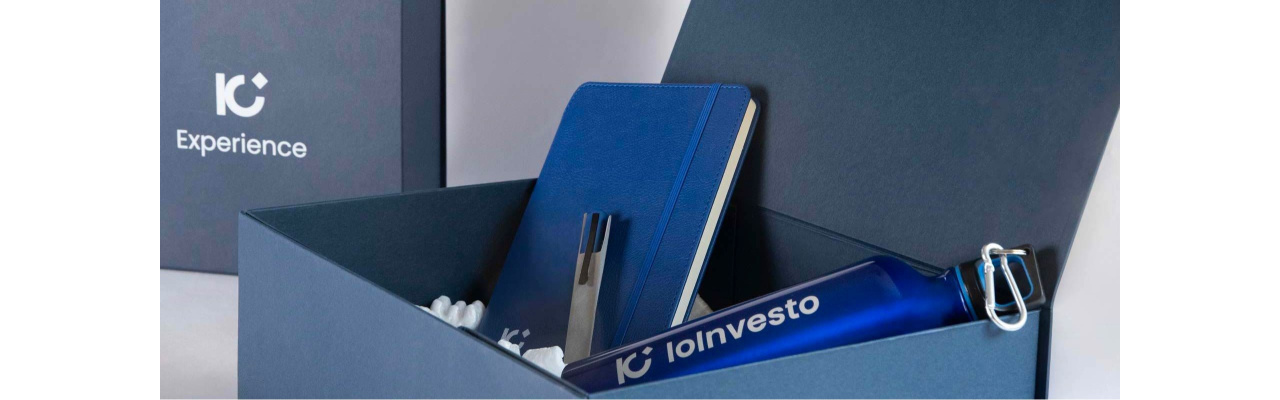 Box di benvenuto contenente un'agenda con copertina rigida e elastico, una penna e una borraccia in acciaio, tutto di colore blu con il logo di un brand
