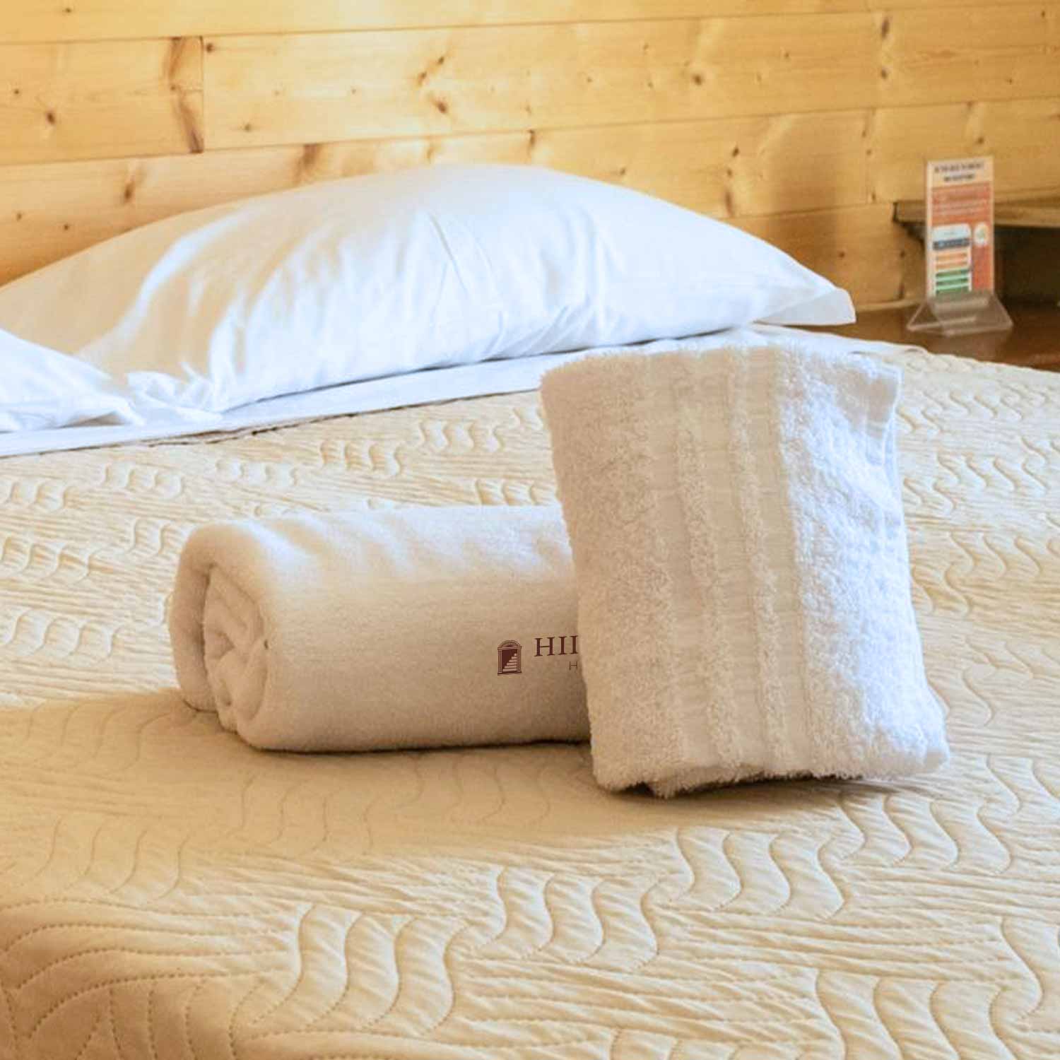 Letto di hotel con lenzuola bianche e asciugamani bianchi arrotolati al centro. 