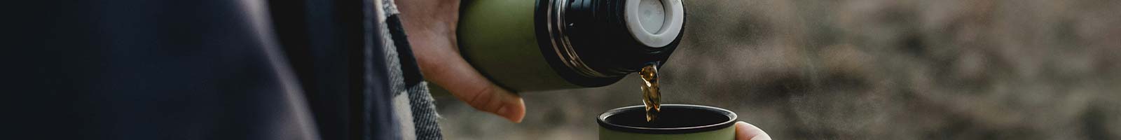 Mani che versano the caldo da un thermos a un bicchiere.