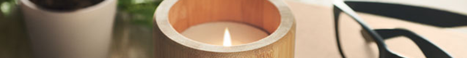 Candela in bambù accesa con accanto un paio di occhiali da vista neri, poggiati su un tavolo di legno chiaro.