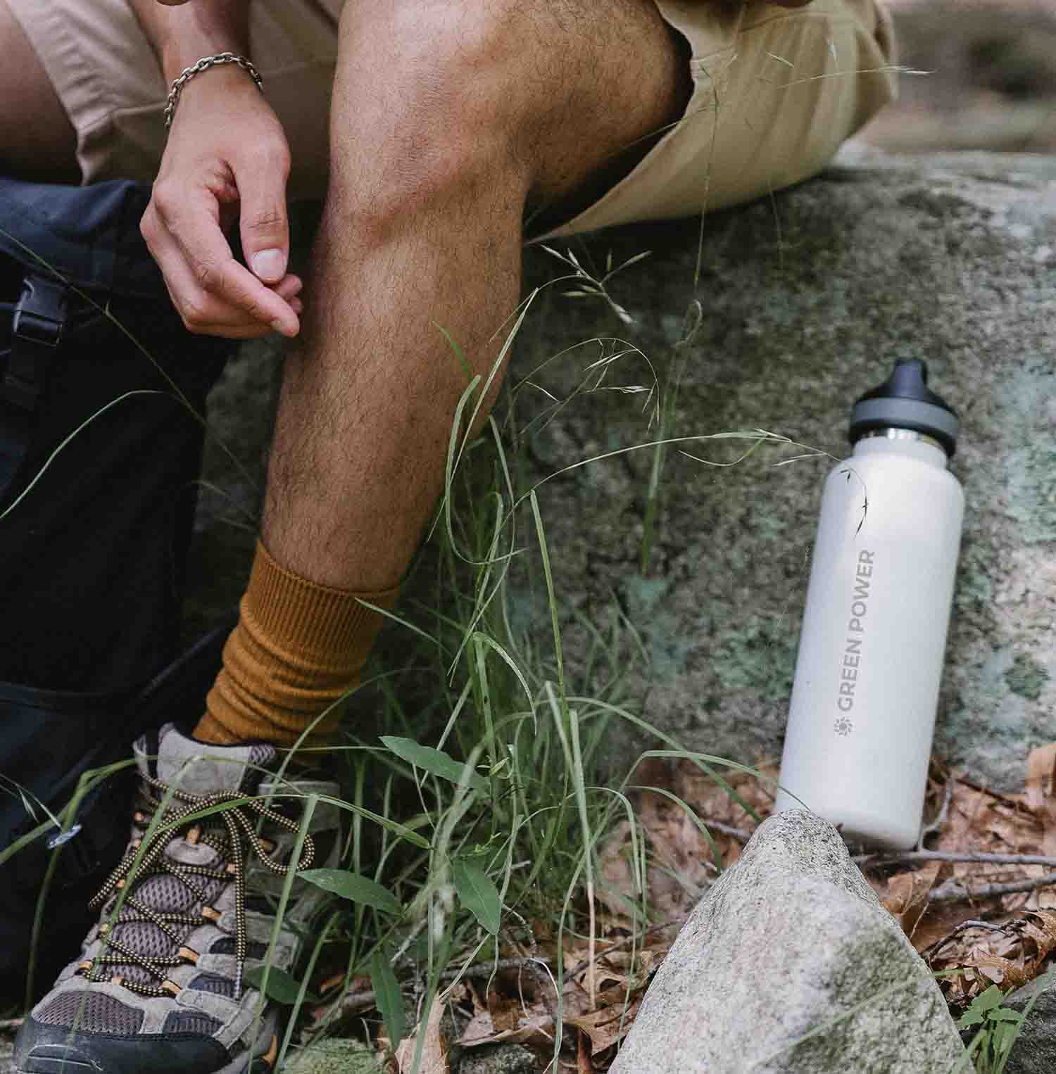 Gambe di un ragazzo nel bosco con accanto una borraccia personalizzata scelta come gadget per team building nella natura