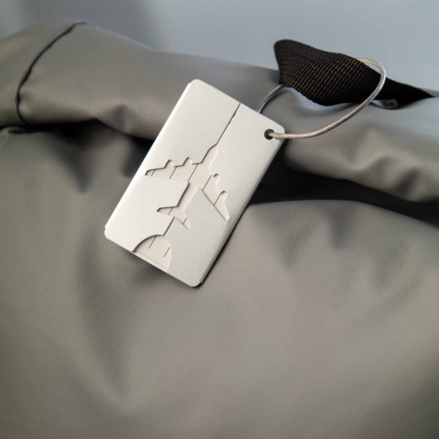 Etichetta per bagaglio in alluminio legata al manico superiore di uno zaino verde militare.